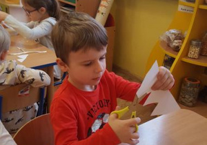 Chłopiec wycina koronę z papieru.